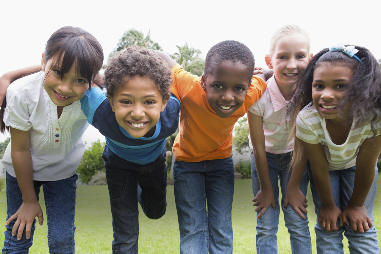Five smiling children lock arms and lean towards the camera in a joyful moment.