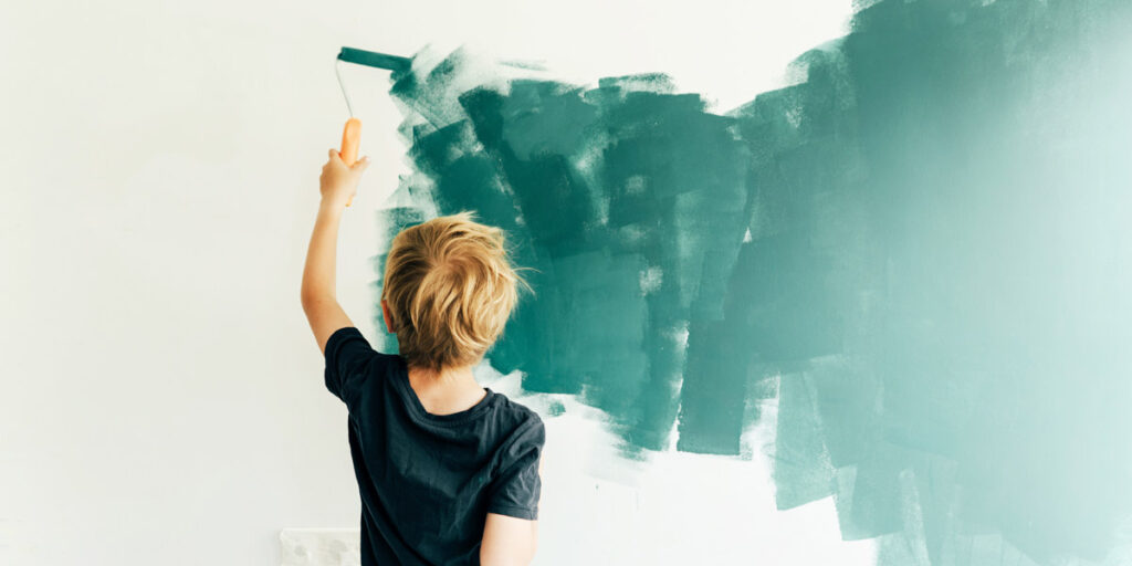 A young boy paints a wall dark green.
