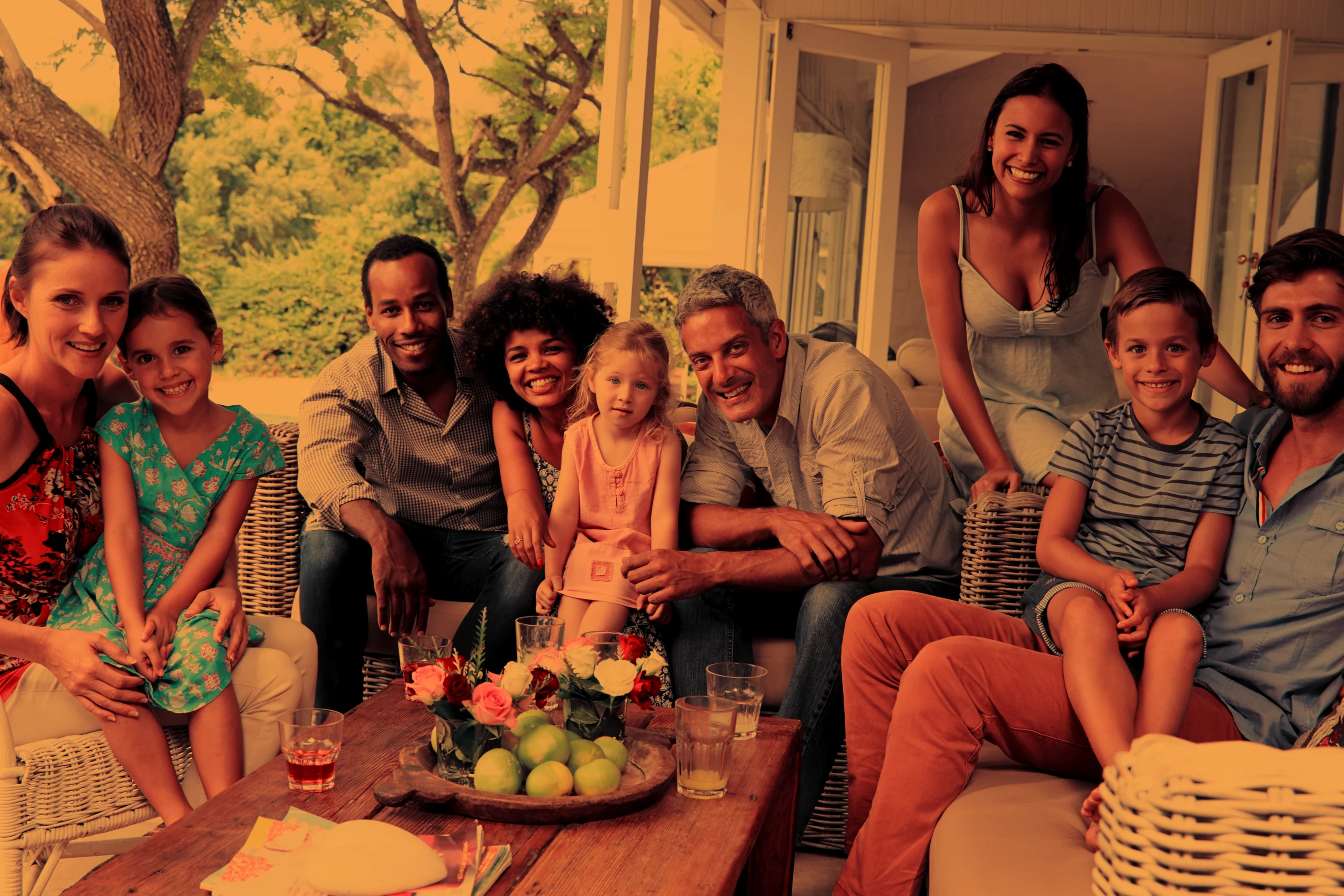 Three generations of two families sitting together on a patio, smiling at the camera