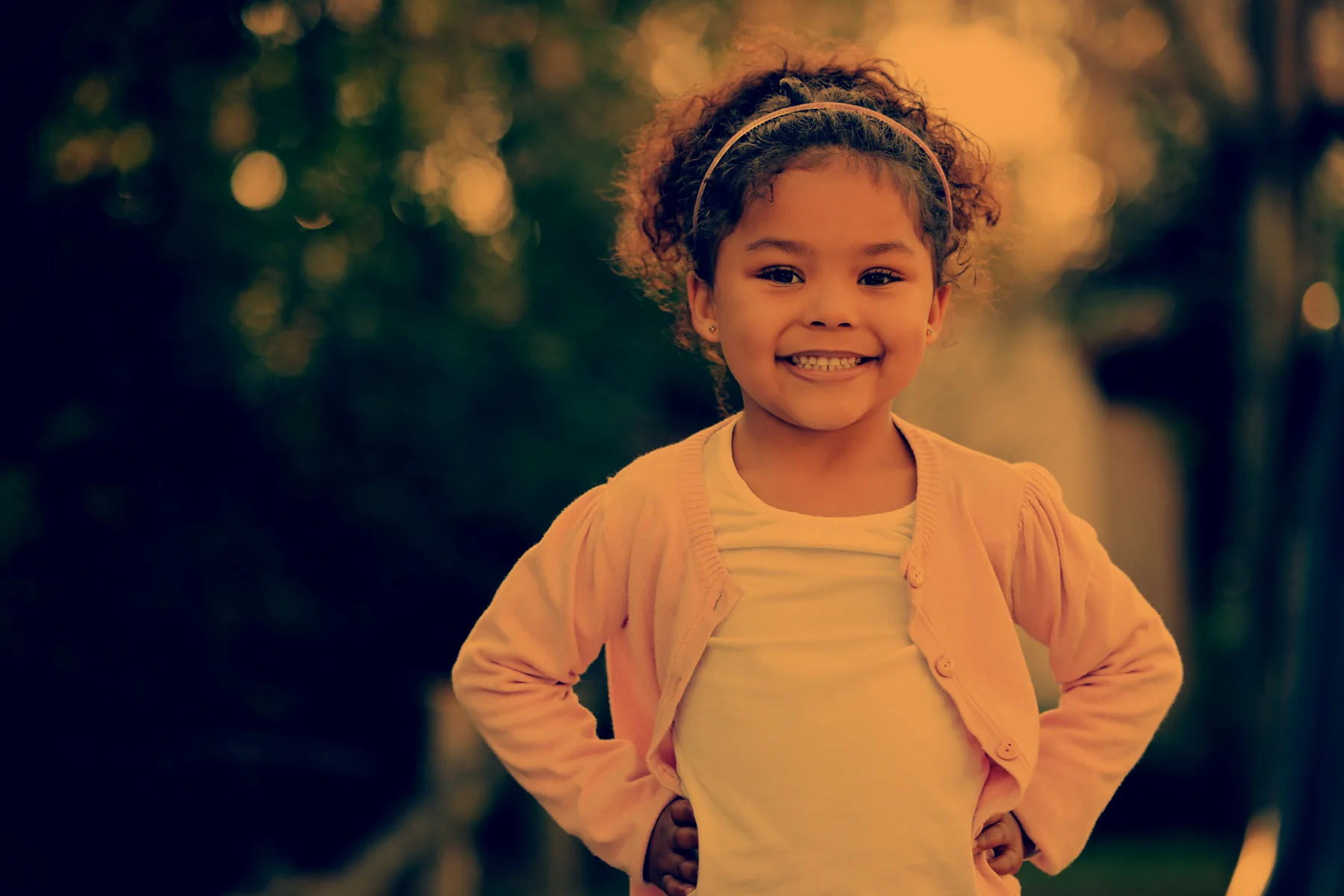 A smiling young girl standing outdoors with her hands on her hips