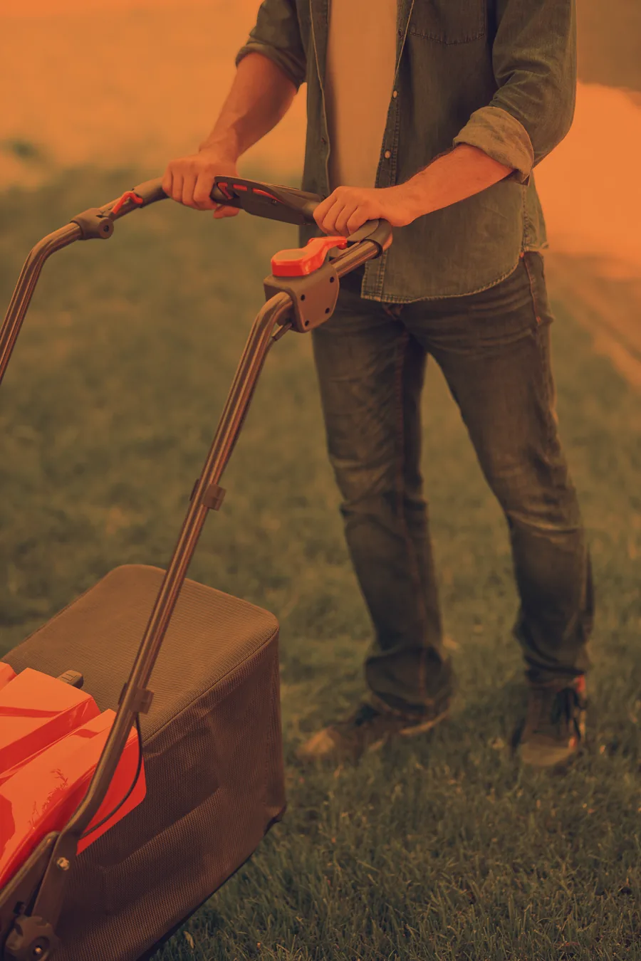 A neighbor pushing a lawn mower across a yard at sunset